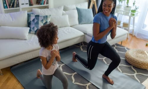 Diverse mother & her daughter wearing a CGM are doing leg exercises in the living room